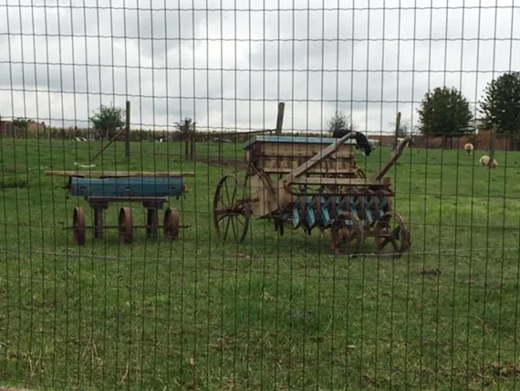 Oude zaaimachine en een blauwe houten kar in de weide